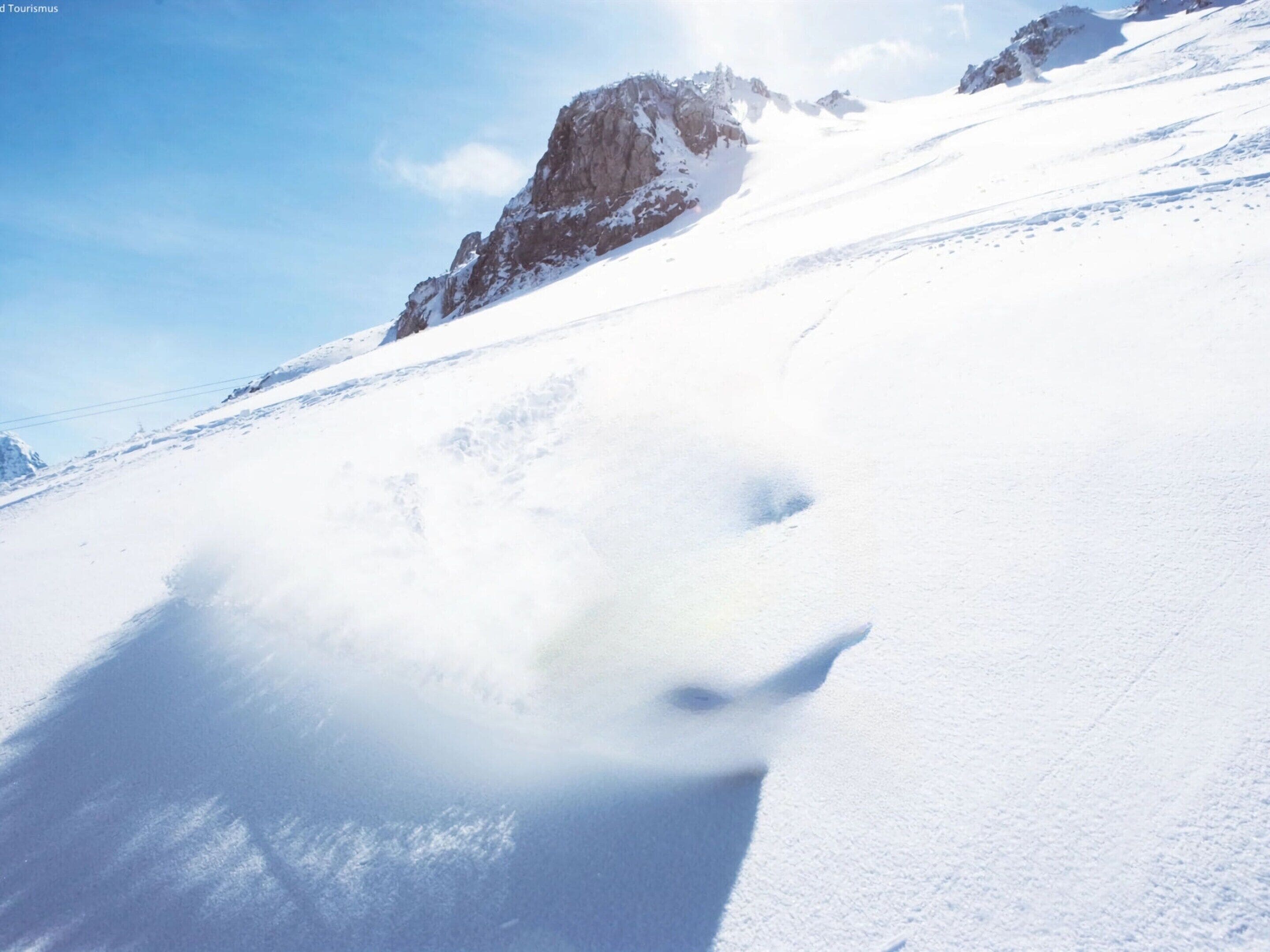 A snow-covered mountain slope with a rocky outcrop in the background.