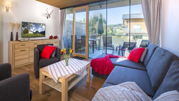 A living room with a sofa, a coffee table, a TV, and a balcony with outdoor furniture. - Bright Mountain Retreat Near Wildkogel Gondola (Neukirchen am Grossvenediger)