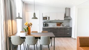 Une cuisine moderne équipée d’un four à micro-ondes, d’une cuisinière et de meubles de rangement aux couleurs sombres. On y trouve une table à manger avec des chaises et un vase de fleurs.