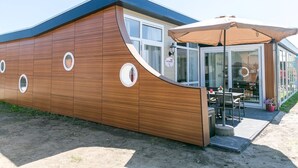 Un bâtiment moderne avec une façade en bois, de grandes fenêtres et un espace extérieur aménagé avec des sièges.