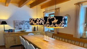 Comedor con una larga mesa de madera, sillas blancas y lámparas colgantes con estampado vaca blanco y negro.