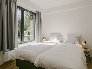 Un dormitorio con un ventanal grande, una cama con ropa de cama blanca, dos lámparas de noche y una mesita redonda.