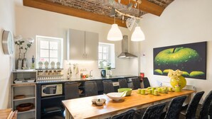 A modern kitchen with a wooden dining table, grey cabinets, and a large green apple painting on the wall. - Located Near Maastricht Towards the Belgium Border (Eijsden)