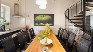 A long wooden table with chairs, a kitchen area with a stove and sink, and a staircase with a metal railing. - Located Near Maastricht Towards the Belgium Border (Eijsden)