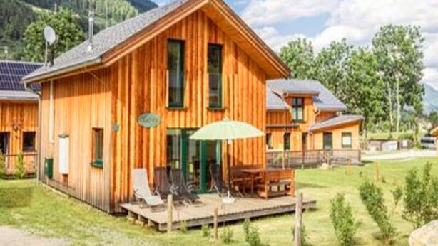 Eine Holzhütte mit einer Terrasse, Sitzgelegenheiten im Freien und einem Bergpanorama.