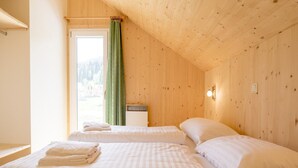 Ein Zimmer mit zwei Betten, einem Vorhangfenster, Holzwänden und einem kleinen Nachttisch.