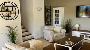 Un salón con sofá, mesa de centro y televisor. Se ve una escalera que conduce a otra habitación.
