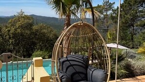 Una silla colgante de mimbre junto a una piscina con vistas despejadas a las montañas.