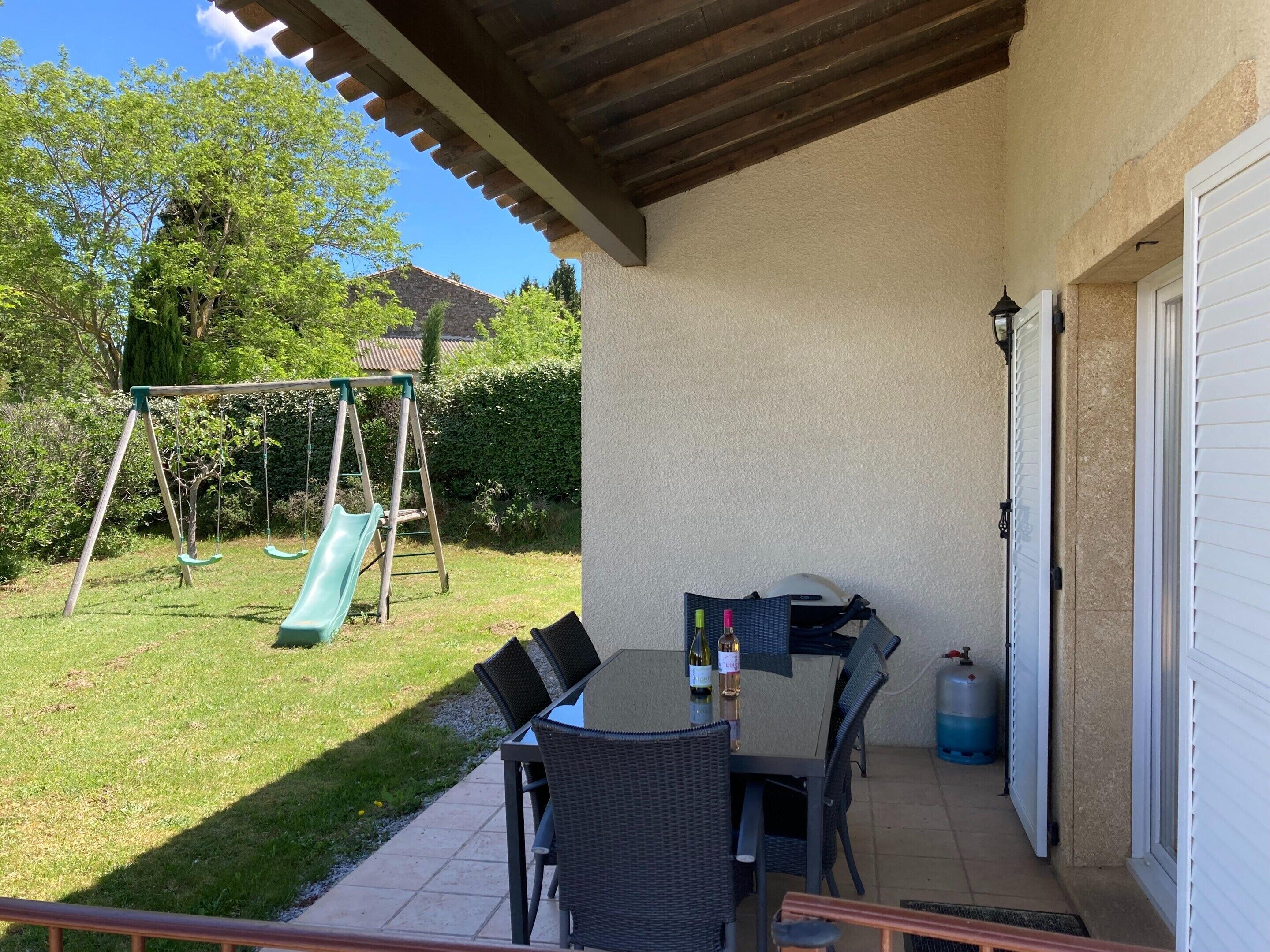 A patio with a table, chairs, a swing set, and a water dispenser.