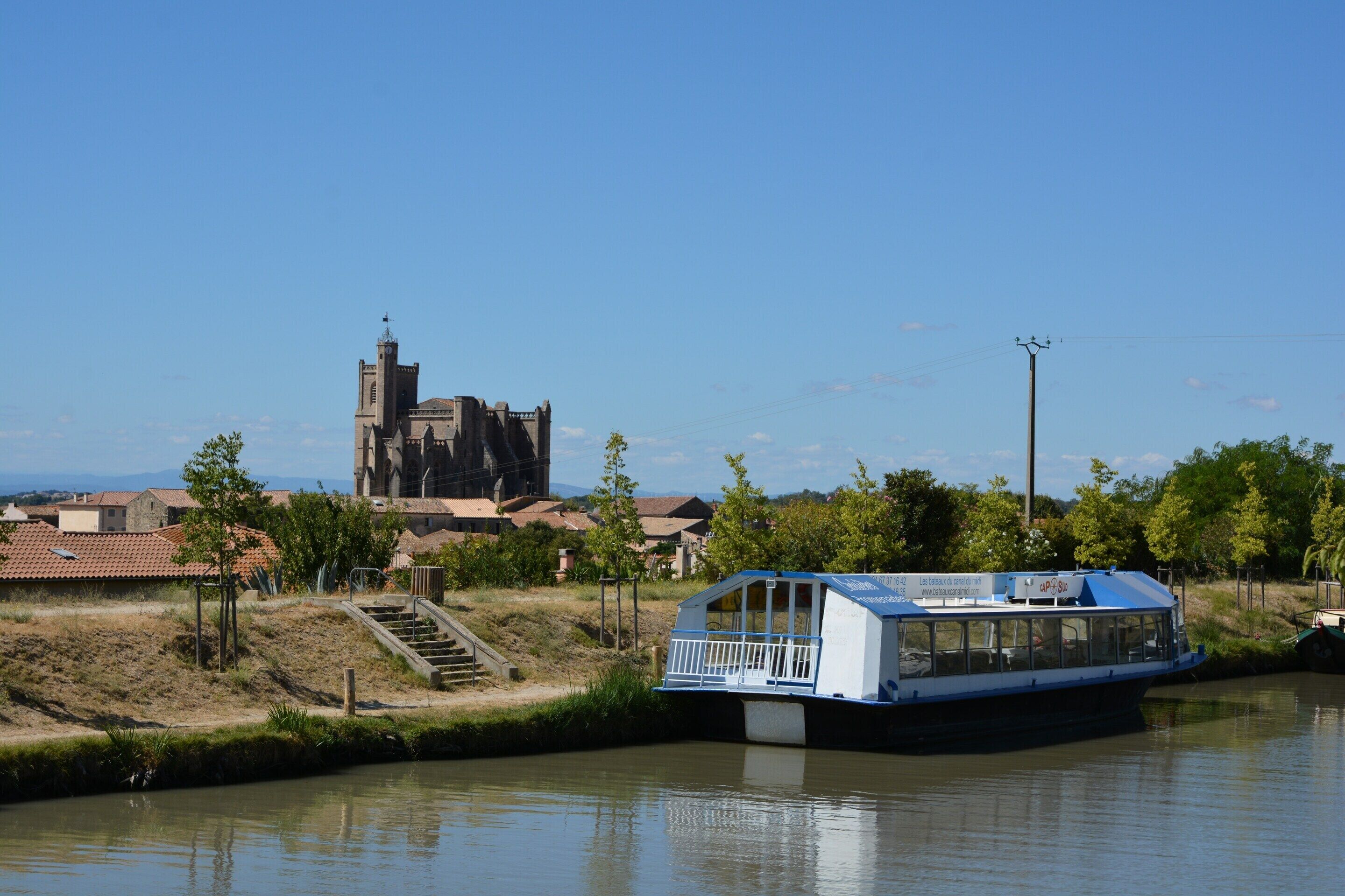 Une rivière avec un bateau amarré près du rivage, une église en arrière-plan et un petit escalier menant au bateau.