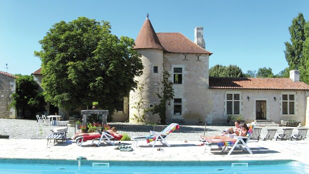 Ein Schwimmbecken mit Liegestühlen und ein Steinhaus mit einem Turm im Hintergrund.