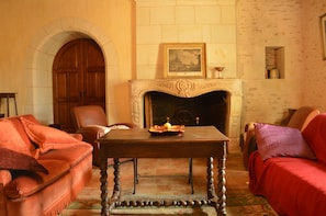 A room with a fireplace, a wooden table, a sofa, and a chair. - Holiday Home in Thurageau With Private Pool (Thurageau)