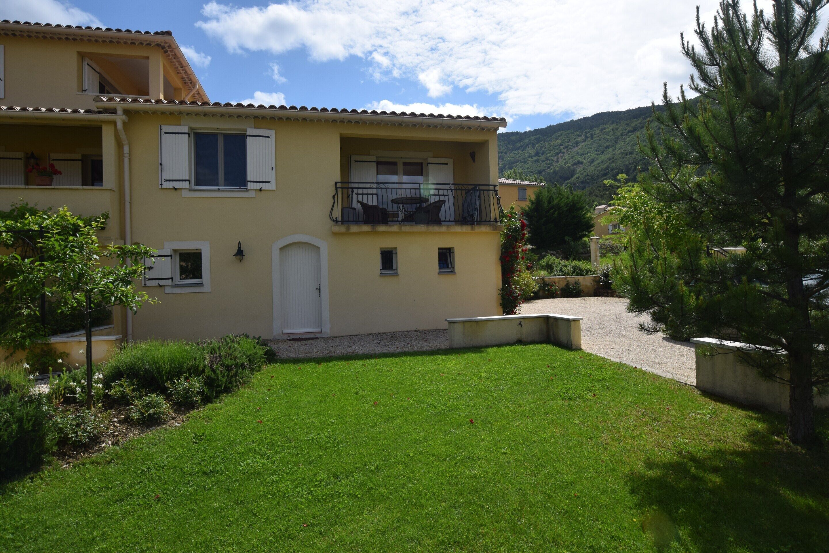 Un immeuble de deux étages doté d’un balcon, d’une porte d’entrée et d’un petit jardin.