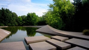 Um parque com um lago tranquilo, degraus de concreto e vegetação exuberante.