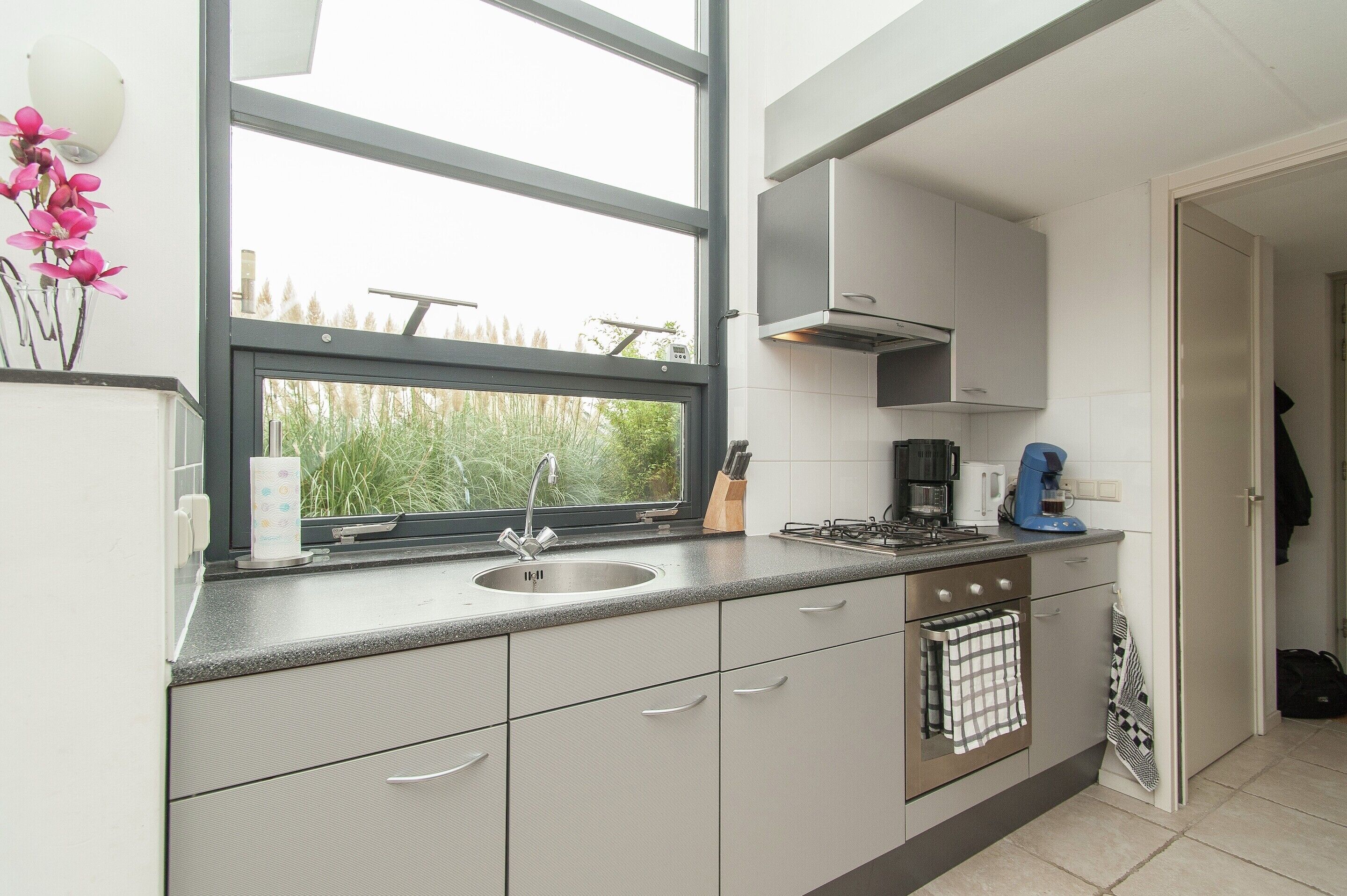 A modern kitchen with a large window, stainless steel appliances, and white cabinetry.
