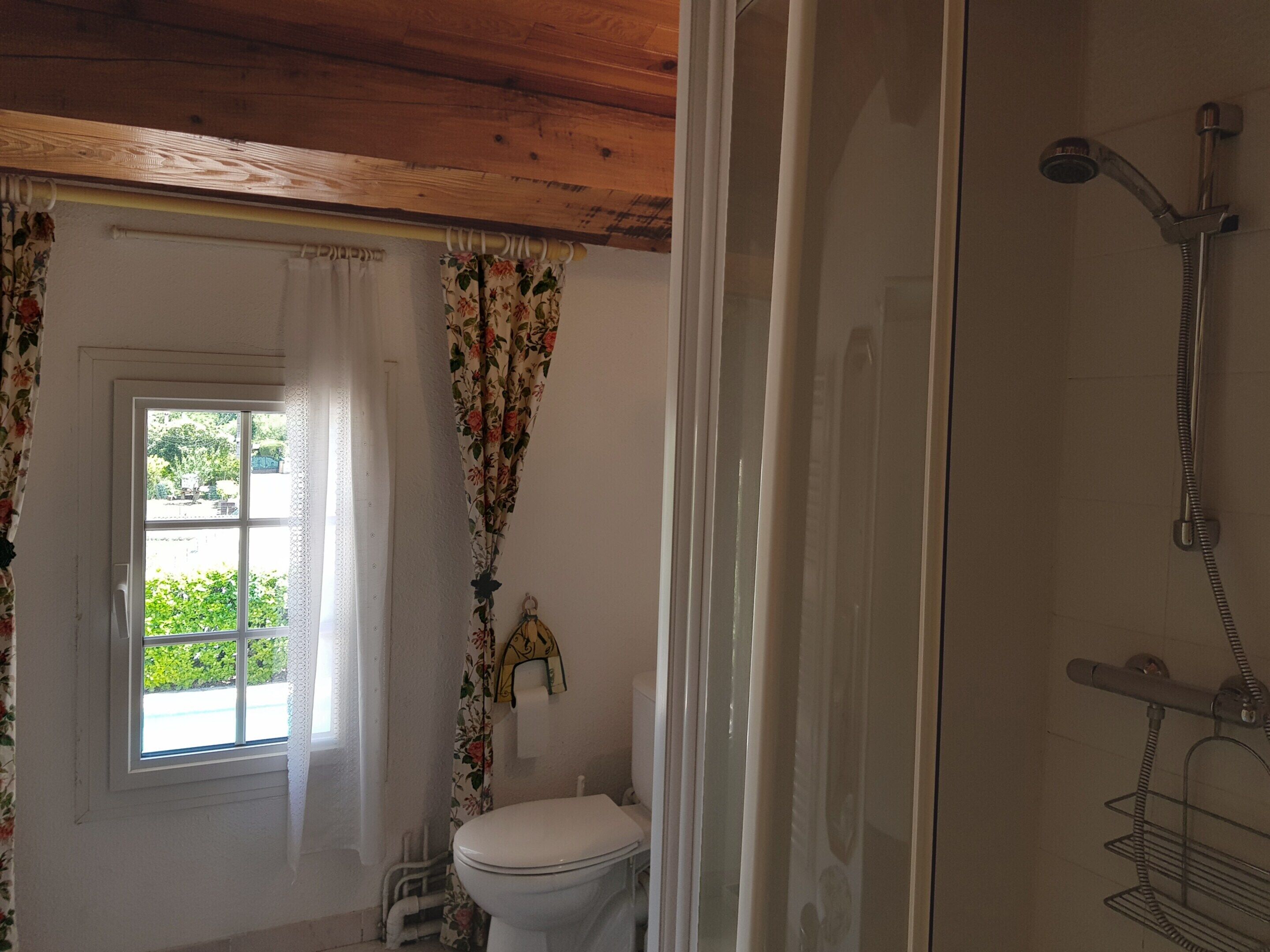 Une salle de bain avec des toilettes, une douche et une fenêtre avec des rideaux.