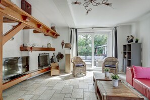 A spacious living area with a fireplace, wicker furniture, and a large window providing a view of the outdoors. - Villa in Bruinisse Near Grevelingenmeer (Bruinisse)