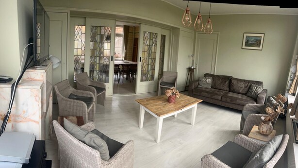 Een woonkamer met rieten meubels, een houten bijzettafeltje, een bank en een televisie.