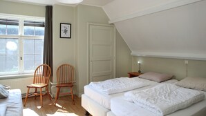 Een slaapkamer met twee bedden, een raam met zonwering, een houten stoel en een witte radiator.