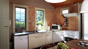 Een compacte keuken met een vaatwasser, magnetron en kookplaat, houten kastjes en een raam met uitzicht op groen.