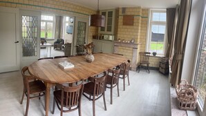 Een eethoek met een grote houten tafel, zes stoelen en een vaas met gedroogde bloemen.