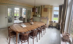 Uma sala de jantar com uma grande mesa de madeira, seis cadeiras e um vaso com flores secas.