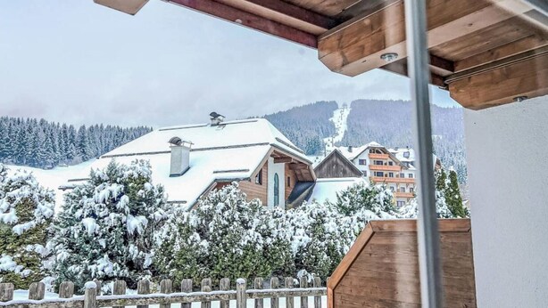 Ein Holzbalkon mit Blick auf einen schneebedeckten Berg und Häuser.