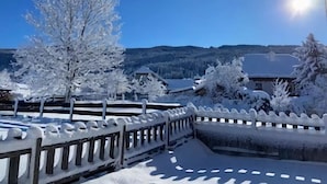 Schneebedeckte Landschaft mit Holzzaun, Bäumen und blauem Himmel.