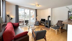 Ein modernes Wohnzimmer mit einer Couch, Sesseln, einem Fernseher und einem Kamin.