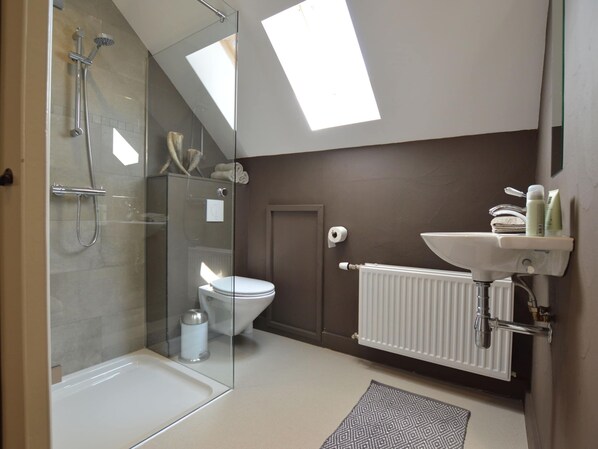 Un bany modern amb dutxa tancada amb vidre, un vàter blanc, un lavabo amb productes de tocador i un radiador.