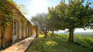 Un sendero conduce a un edificio con ventanales arqueados y un porche cubierto, rodeado de árboles y vistas del paisaje.