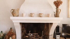Una chimenea con repisa blanca, leña y un estante con tazas de cerámica.