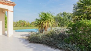 Een zwembadgedeelte met een helderblauwe lucht, omringd door weelderige begroeiing en een gebouw met een pannendak.