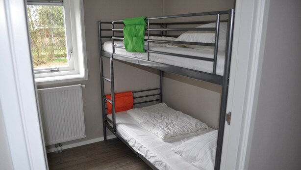 Une chambre avec un lit superposé, une fenêtre, un radiateur et un plancher en bois.