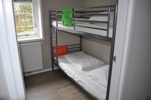 A bunk bed room with a window, a radiator, and a wooden floor.
