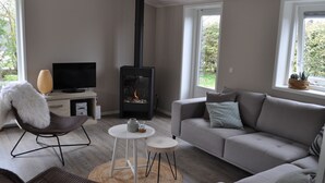 Un salon moderne avec une cheminée, un canapé, un fauteuil, un téléviseur et une fenêtre donnant sur un paysage verdoyant.