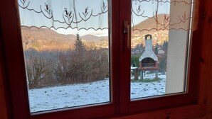 A room with a table featuring a bottle of wine and a menu, a window with a view of a snowy landscape and a church, and wooden walls. - Apartment in the Vosges (Saint-Maurice-sur-Moselle)