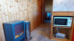 A room with a wood-paneled wall, a blue heater, a stainless steel trash can, and a microwave on a wooden shelf. - Apartment in the Vosges (Saint-Maurice-sur-Moselle)