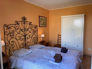 A bedroom with a bed, a nightstand, a chair, a wardrobe, and a wall-mounted picture. - Montbrun Vineyard Escape (Montbrun-des-Corbières)