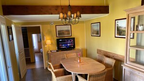 A dining area with wicker chairs, a wooden table, a television, and a chandelier. - Montbrun Vineyard Escape (Montbrun-des-Corbières)