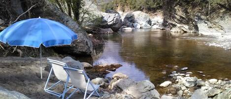 A river with rocks, a blue umbrella, and a chair.