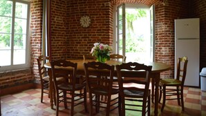 A dining area with a brick wall, a clock, a table with chairs, and a refrigerator. - House Near Merlimont-plage and Historic Abbey (Gouy-Saint-Andre)