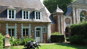 A brick building with a garden, a small table with chairs, and a decorative archway. - House Near Merlimont-plage and Historic Abbey (Gouy-Saint-Andre)