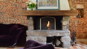 A fireplace with a framed picture above it, a brick wall, and a purple sofa in the foreground. - House Near Merlimont-plage and Historic Abbey (Gouy-Saint-Andre)