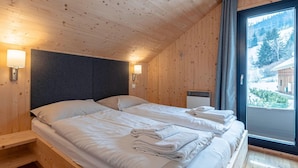 Ein Zimmer in einer Holzhütte mit zwei Betten, einer Heizung und einem Fenster mit Blick auf einen Wald.