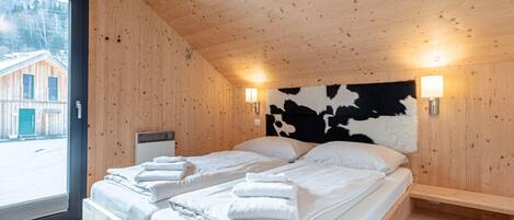 A wooden cabin room with a bed, two wall-mounted lights, and a window overlooking a building.