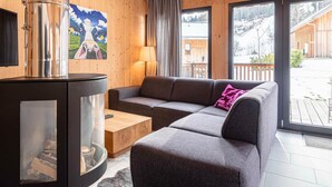 Ein gemütliches Wohnzimmer mit einer Couch, einem Couchtisch, einem Kamin und großen Fenstern mit Blick ins Freie.