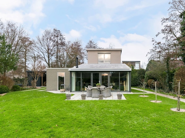 A modern house with a glass conservatory, a well-maintained lawn, and a garden with a few trees.