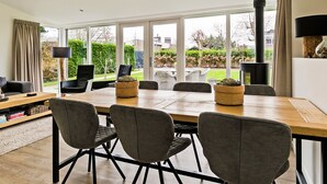 A spacious dining area with a large table and chairs, a fireplace, and a view of the garden through large windows. - Villa Near Veerse Meer With Garden Views (Kamperland)