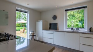 A modern kitchen with a large island, white cabinetry, and a window overlooking a garden. - Villa Near Veerse Meer With Garden Views (Kamperland)